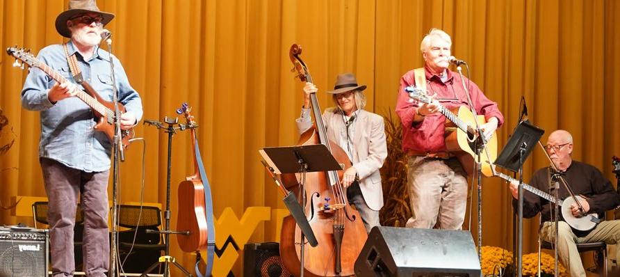 a group image of the music group 'buffalo run' performing onstage at the church mckee arts center.  The background is a golden curtain, and they are playing on various acoustic string instruments, cast in bright light